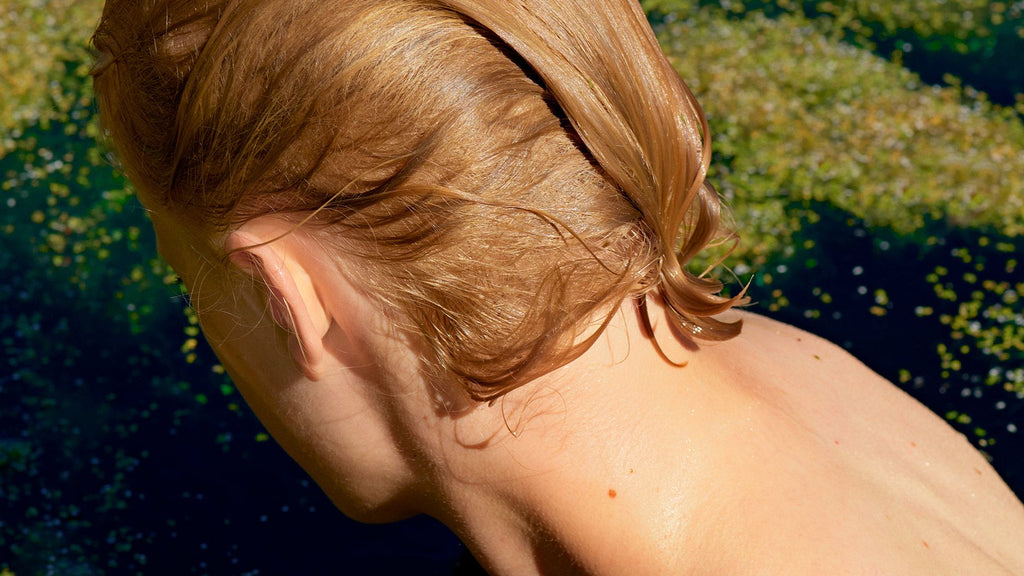 Back of model's head and neck with short light coloured hair surrounded in green nature